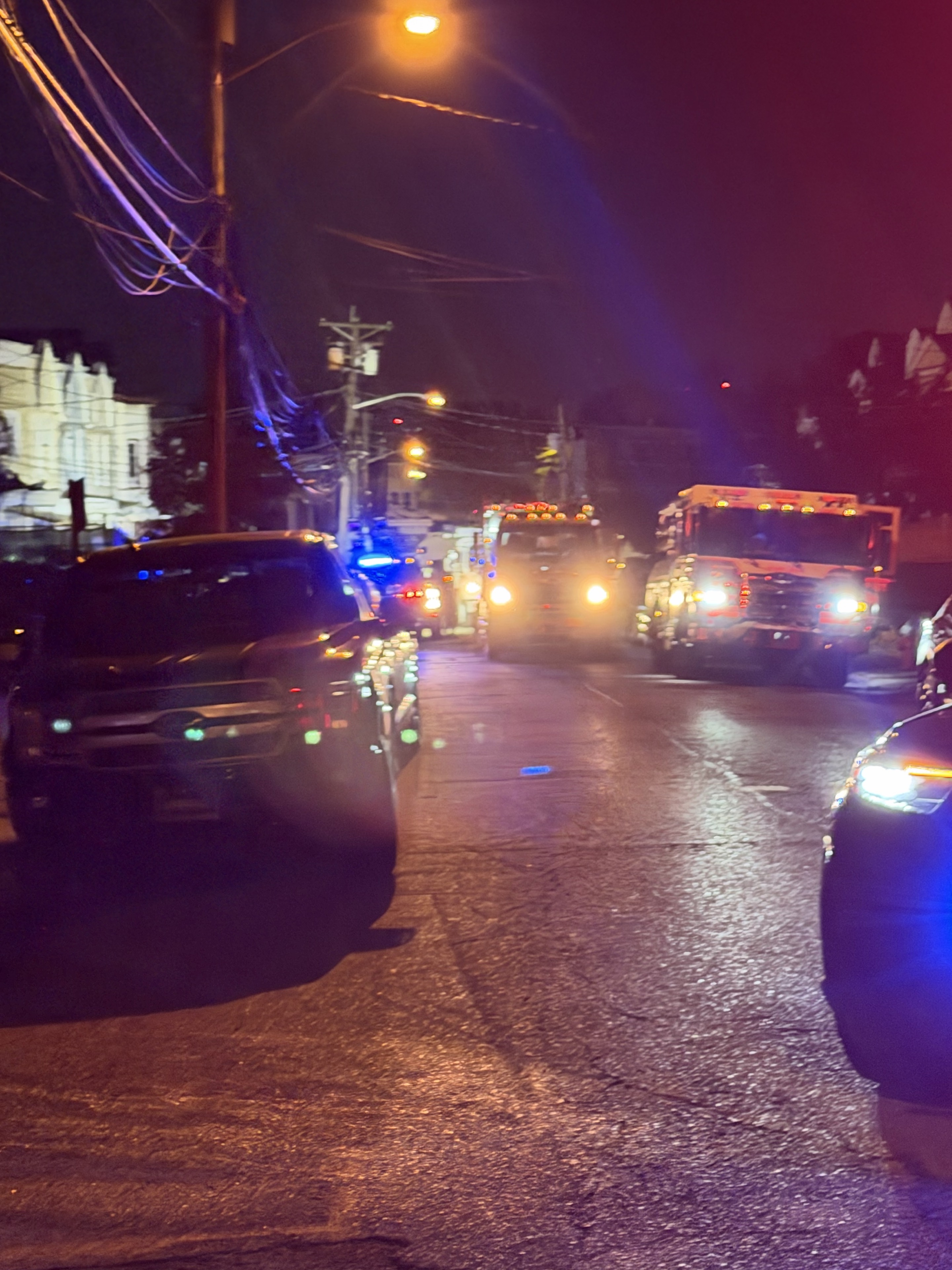 Emergency vehicles with lights on along Boyd Avenue at night, with a dark parked SUV in the foreground.